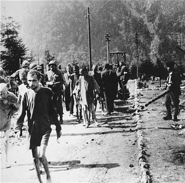 American soldiers walk among emaciated survivors along a road in the Ebensee concentration camp.jpg