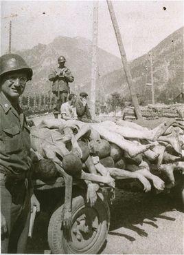 An American colonel poses next to a wagon loaded with the bodies of former prisoners at the newl.jpg