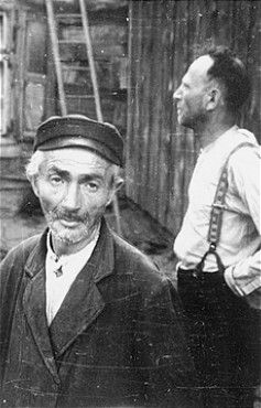 Two Jewish men stand outside a wooden building in Konskowola.jpg