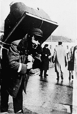 A young Jewish man wearing an armband, carries a large piece of furniture on his back into the K.jpg