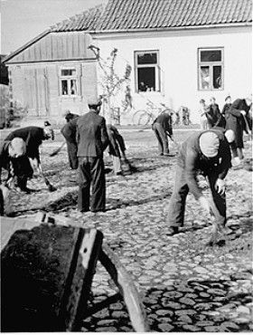 Jewish men are forced to sweep the pavement in the town square of Raciaz with short brooms.jpg