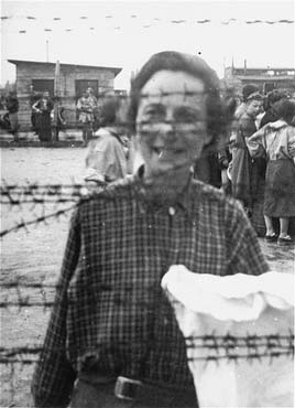 Portrait of a female survivor of Mauthausen standing behind the barbed wire fence.jpg