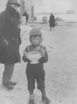 In the Kovno ghetto, a child carries a bowl of soup and holds food ration tickets.jpg