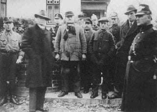 Jews arrested during Kristallnacht stand under guard before being deported to the Sachsenhausen .jpg