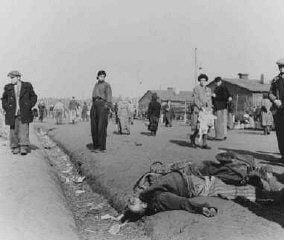 Soon after liberation, camp survivors walk amidst dead bodies.jpg