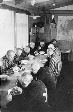 Sachsenhausen prisoners, wearing different types of uniforms, eat a meal in the mess hall of the.jpg