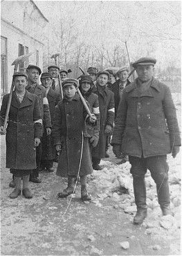 Olkusz, Kutno, Wisznice, Raciąż and Other Jewish Ghettos, 1939-1942 - Escorted by a Pole, a group of Jewish men and youth from Olkusz march to a work site carrying sh