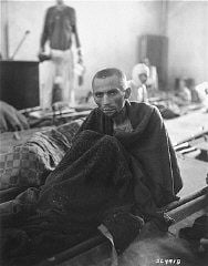 An emaciated survivor wrapped in a blanket sits up on a stretcher in the newly liberated Gusen c.jpg