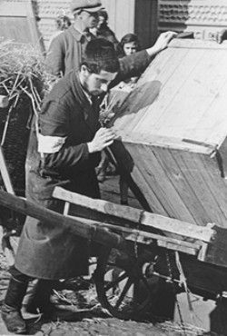 A religious Jewish youth loads a large crate onto a cart in the Krakow ghetto.jpg