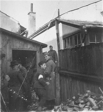 German soldiers stand guard while a group of religious Jews is forced to move a pile of wood.jpg