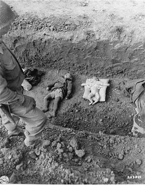 An American soldier stands above the corpses of children that are to be buried in a mass grave.jpg